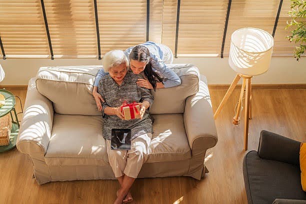 An older Asian woman receiving a gift from a younger family member at home.