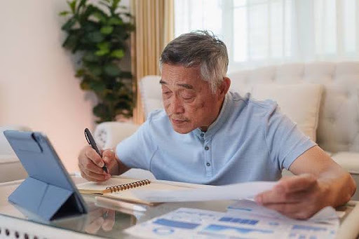 Older Asian man reviewing financial documents and retirement income sources for potential tax obligations.
