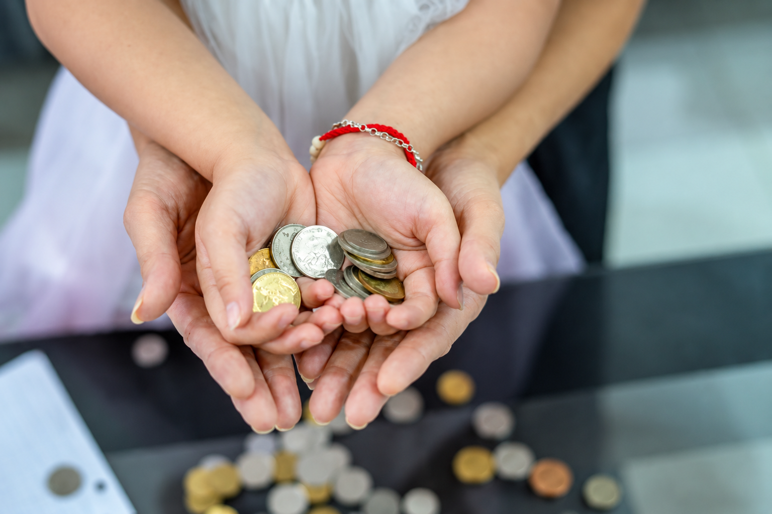 Adult guiding a child with coins, representing the importance of financial literacy and money management in Malaysia.